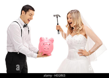 Young groom holding a piggybank with a bride preparing to break it with a hammer isolated on white background Stock Photo