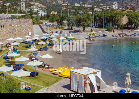 AGIOS NIKOLAOS, GREECE - AUGUST 2, 2012: Tourists swim in the Mediterranean sea on the beach of one of the hotels with plenty of sun loungers and para Stock Photo