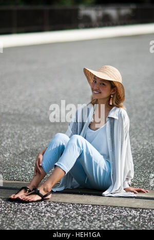 Happy, beautiful Japanese girl wearing a straw hat and smiling at the camera is sitting on the floor