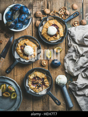 Plum and walnut crostata pie with ice-cream scoops in individual cast iron pans over rustic wooden table, top view. Slow food concept Stock Photo