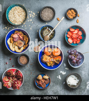 Ingredients for healthy breakfast over grey stone background, top view, square crop. Fresh and dried fruit, chia seeds, oatmeal, nuts, honey. Clean ea Stock Photo