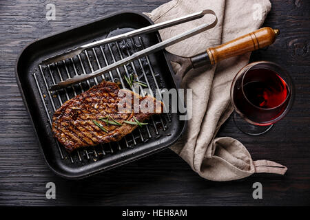 Grilled Steak Striploin in grill iron pan and red wine on black burned wooden background Stock Photo