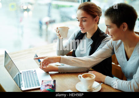 Two girls having coffee and looking through pictures in cafe Stock Photo