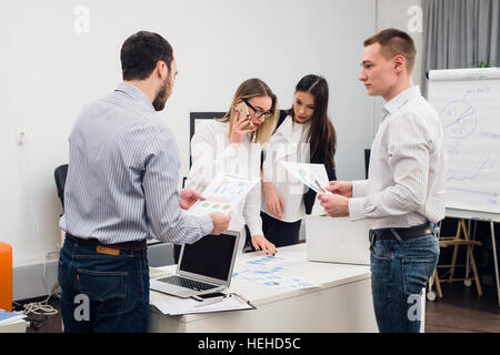 Young business people sitting in office during meeting and discussing with paperwork using laptops Stock Photo