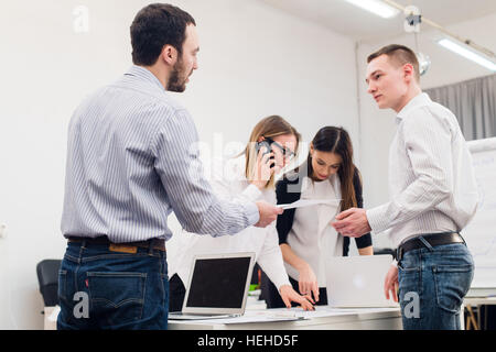 Group of four diverse cheerful co-workers taking self portrait and making funny gestures with hands at small office Stock Photo