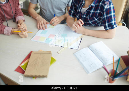 Desk with notebooks and students of design faculty carrying out assignment Stock Photo