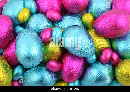 Pile of foil wrapped chocolate easter eggs in pink, blue & lime green. Stock Photo