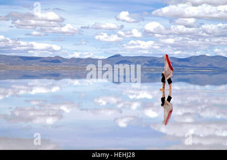 Woman walking in the clouds, mirror reflection in the water at the Uyuni Salt Flats Bolivia Stock Photo