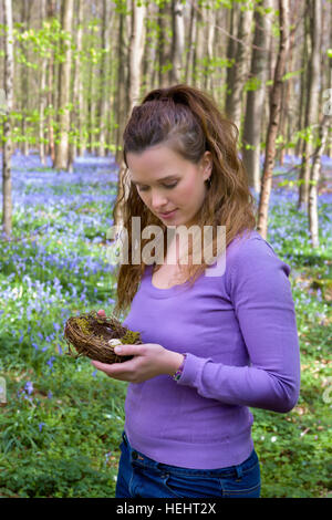 Pretty young woman holding a bird's nest in a bluebells springtime forest Stock Photo