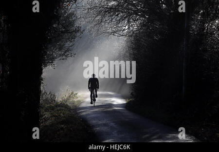 A man cycles through some early morning fog on a country lane near Copthorne in West Sussex. Stock Photo