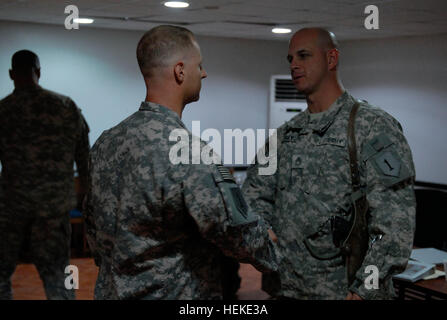 Sgt. 1st Class William Mackey, right, a platoon sergeant with 1st “Dragon” Battalion, 63rd Armor Regiment, 2nd “Dagger” Brigade, 1st Infantry Division, United States Division – Center and an Arkansas native, congratulates Staff Sgt. Joshua Bell, center, a gunnery sergeant with 1st “First Lightning” Battalion, 7th Field Artillery Regiment, 2nd AAB, 1st Inf. Div., USD-C and a Santa Rita, Guam, native, on his acceptance into the Sgt. Audie Murphy Club Sept. 23 at Camp Liberty, Iraq. Bell, who has earned two Purple Hearts during his current deployment, was asked a range of questions about himself  Stock Photo