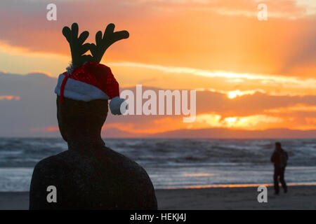 Sunset over Crosby, Liverpool, UK. 22nd Dec 2016. Weather.  A man walking on the beach at sunset, passes 'Antony Gormley's' Iron Men sculptures on the stunning north west coastline.  These spectacular sculptures are on Crosby beach near Liverpool.   'Another Place' consists of 100 cast-iron, life-size figures spread out along three kilometres of the foreshore, stretching almost one kilometre out to sea.  © Cernan Elias/Alamy Live news Stock Photo