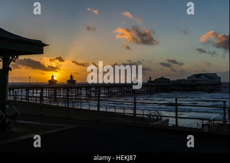 Blackpool, UK. 22nd Dec, 2016. The sun sets over Blackpool's North Pier on a bitterly cold day from a deserted promenade as a prelude to the forecast 'Storm Barbara', which is due to hit the UK tomorrow. The Met Office is expecting gusts of up to 90mph in places during the storm. ©Andy Gibson/Alamy Live News. Stock Photo