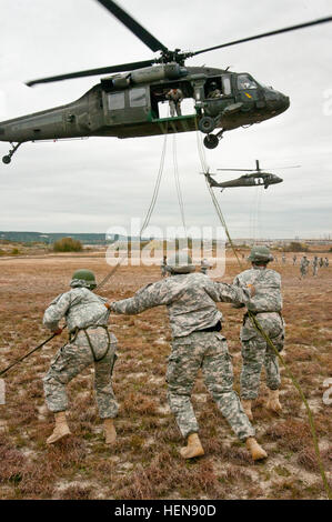 Fort Hood Air Assault instructor Sgt. Anthony Eashman (center), from San Francisco, Cali., guides two students during Phase Three rappel testing, Nov. 20, 2013. Air Assault School qualifies soldiers to conduct airmobile and air assault helicopter operations, to include aircraft orientation, sling load operations, proper rappelling techniques and fast-rope techniques. The school itself is 10 days of rigorous, fast paced training. The high standards of the school require the student to take part in a 12-mile march with rucksack in under three hours on the morning of graduation to be awarded thei Stock Photo