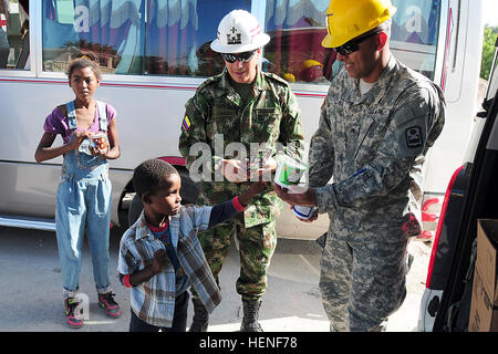Sgt. Miguel Coss, a native of San Juan, Puerto Rico, hands out cereal and chocolate candy to a Dominican boy along with Colombian Army Lt. Col. Jose Manuel Gomez Valenzuela at a construction site in Barahona, Dominican Republic, April 26.  Coss is a Puerto Rico National Guardsmen currently assigned to the United States Army South Task Force Larimar, and is participating in the 2014 Beyond the Horizon (BTH) humanitarian mission at the Dominican Republic. Task Force Larimar is currently conducting engineering works at five different sites by constructing three medical clinics and two schools in  Stock Photo