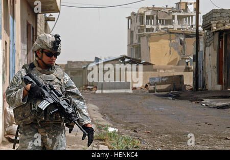 Spc. Vencent Hashimoto, an infantryman in 1st Platoon, Company D, 1st Battalion, 8th Infantry Regiment from Fort Carson, Colo., patrols through the streets of Mosul, Iraq, April 1, during a clearing operation. The car bombed Iraqi Army combat outpost, now a skeleton building behind him is a looming reminder of the dangers that still linger in Mosul. During the raid IA and coalition forces discovered and destroyed several bags of homemade explosives, bomb making materials and a car bomb factory. Infantry Soldiers conduct Mosul raid through rain and shine 83273 Stock Photo