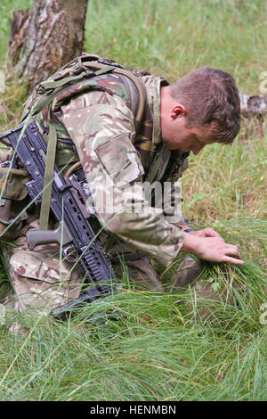 British Army Royal Military Academy Sandhurst cadet Michael Harrison adds grass to camouflage his helmet before going through the individual live-fire exercise. Sandhurst and West Point Military Academy cadets completed their second day of a joint two-week field exercise with live-fire training. The exercise consisted of individual and squad movements on range 204 at the Grafenwoehr Training Area at the U.S. Army's 7th Army Joint Multinational Training Command, July 8. Cadets from Sandhurst are completing their final field exercise and the 50 West Point cadets are completing their leadership d Stock Photo