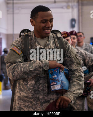 Pfc. Ezekiel Polite, a paratrooper with the 82nd Airborne Division, gives his toy to one of the elves in exchange for his lottery ticket at the 17th Annual Randy Oler Memorial Operation Toy Drop, at Green Ramp, Pope Army Airfield, Fort Bragg, N.C., Dec. 5, 2014. Polite was the first paratrooper in line at 2:45 p.m. the day before the lottery drawing. Operation Toy Drop is the world’s largest combined airborne operation with seven allied partner nation paratroopers participating with seven allied partner nation paratroopers participating and allows Soldiers the opportunity to help children in n Stock Photo