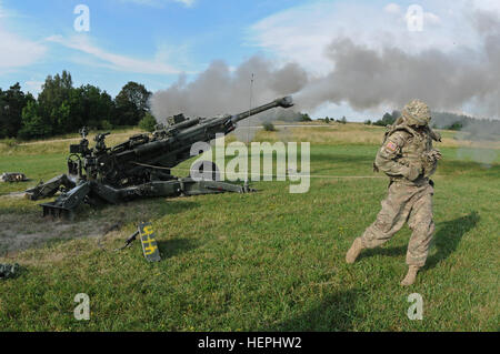 Pfc. Brent Rhodes, a cannon crew member assigned to Alpha Battery, Field Artillery Squadron, 2nd Cavalry Regiment, fires a M777A2 Howitzer weapons system during an artillery demonstration, where they fired an XM1156 Precision Guidance Kit fuse for the first time in the Regiment's history at Grafenwoehr Training Area located near Rose Barracks, Germany, July 24, 2015. The demonstration allowed the Regiment to participate in new equipment training where the PGK fuse (which has global positioning system capabilities that aim to increase the accuracy of High Explosive and Rocket-Assisted Projectil Stock Photo