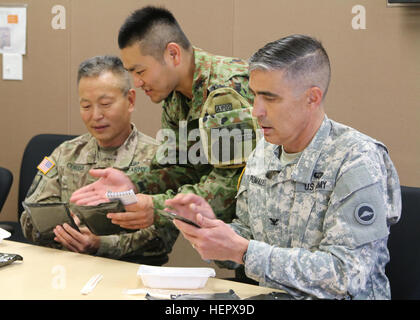 Brig. Gen. Stephen K. Curda (left), Commander, 9th Mission Support Command, Japan Ground Self-Defense Force (JGSDF) service member and Col. Luis Pomales, director, Army Reserve Engagement Team-Japan, share a Meal-Ready-to-Eat lunch at Sagamihara Depot Mission Training Complex during exercise Imua Dawn 2016, Sagamihara, Japan, June 18, 2016.  Imua Dawn 2016 provides opportunities for U.S. and Japanese forces to come together and train for potential real world events, better preparing them in supporting regional populations in all Humanitarian Assistance and Disaster Relief (HADR) and Noncombata Stock Photo