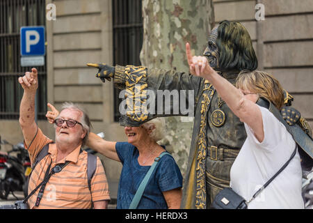 Three tourists having fun while pointing in the air with a street performer in on Las Ramblas, Barcelona, Spain. Stock Photo