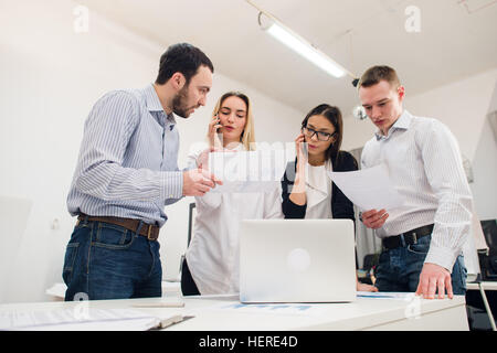 Perfect creative team. Group of four cheerful young people looking at camera with smile while leaning to the table in office Stock Photo