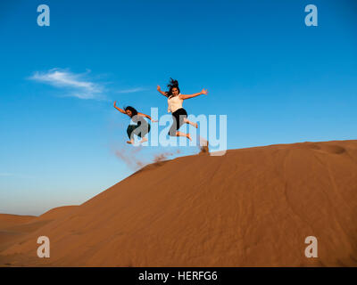 Two young women jumping from sand dune in desert, Sharqiya Sands or Wahiba Sands, Al Raka, Oman Stock Photo