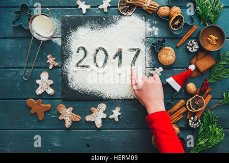Girl making gingerbread men cookies and writing 2017 in icing sugar Stock Photo