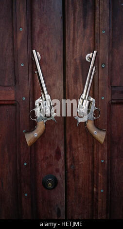 Pistols serve as door pulls on a rustic door in Washington. The guns are the type once used by cowboys in the Old West. Stock Photo
