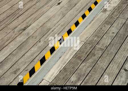 Detail of wooden pedestrian walkway and a black and yellow tape placed on the ground warning off stairs in order to avoid any accident while walking. Stock Photo