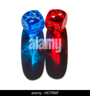 Red and blue transparent plastic dice with shiny shadows. Two tiny dice in sunlight with long colorful shadow cones. Stock Photo