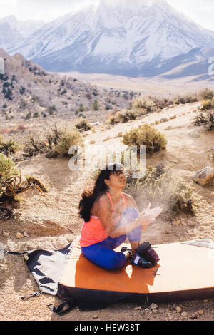 Woman sitting on bouldering mat applying climbing chalk, Buttermilk Boulders, Bishop, California, USA Stock Photo