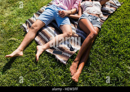 Young couple relaxing outdoors, lying on blanket on grass, holding hands, low section Stock Photo