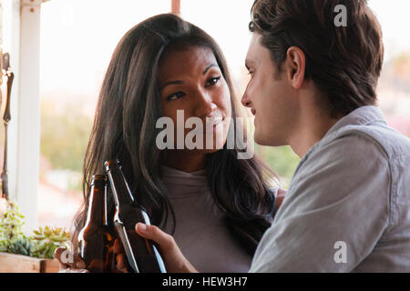 Young couple sitting on veranda, holding beer bottles Stock Photo