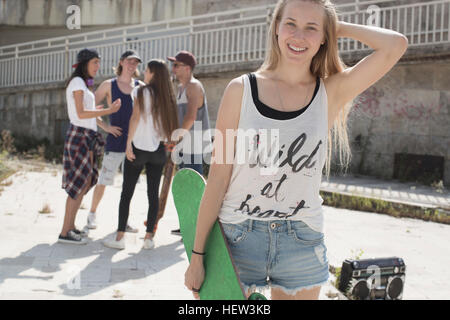 Skateboarder in tank top with wild at heart slogan, friends in background Stock Photo