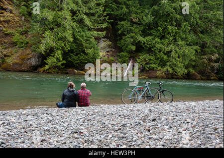 Rear view of couple on riverbank looking away, Packwood, Washington, USA Stock Photo