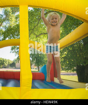 Boy jumping on bouncy castle looking at camera smiling Stock Photo