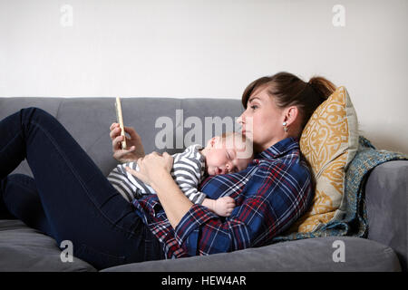 Mother with baby boy lying on sofa looking at smartphone Stock Photo