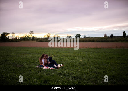 Romantic couple relaxing on picnic blanket in field at sunset Stock Photo