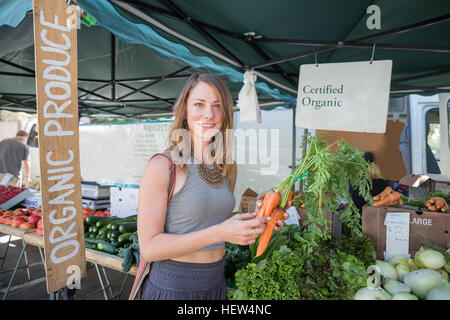 Woman at fruit and vegetable stall holding carrots Stock Photo