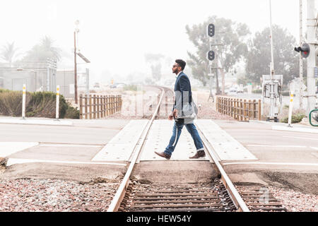 Young man walking across level crossing, side view Stock Photo