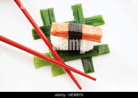 Sushi Nigiri, made with imitation crab meat and rice wrapped in nori seaweed and placed beside red chopsticks on interwoven leek Stock Photo