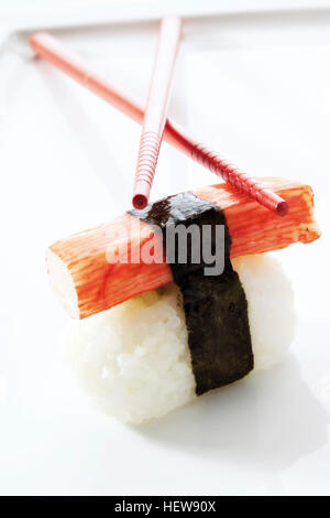 Red chopsticks resting on sushi, Nigiri, Surimi piece made of imitation crab meat and rice wrapped in nori seaweed Stock Photo
