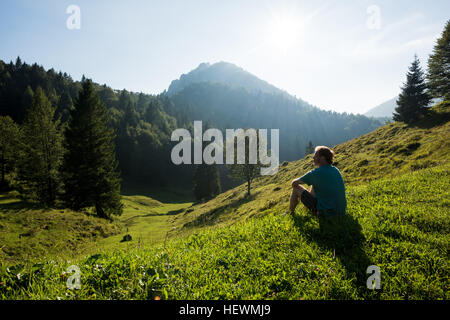 Man sitting on hillside looking away, Passo Maniva, Italy Stock Photo