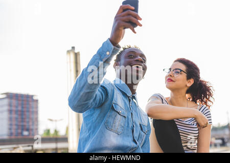 Couple using smartphone to take selfie, Milan, Italy Stock Photo