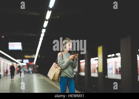 Young woman using smartphone  on railway platform at night Stock Photo