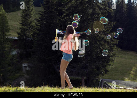 Young woman blowing bubbles in field, Sattelbergalm, Tirol, Austria Stock Photo