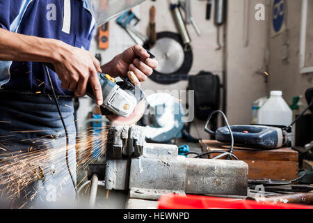 Mid section of young man using angle grinder in repair workshop Stock Photo