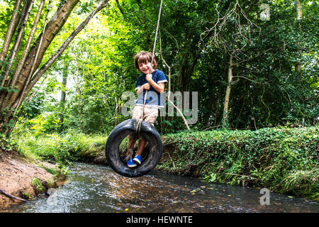Boy on tyre using over river Stock Photo