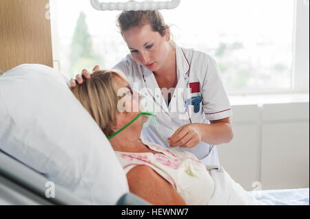 Nurse tending to patient in hospital bed wearing oxygen mask Stock Photo